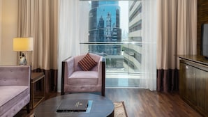 A modern hotel room with a round coffee table, a plush armchair, a sofa, a TV, and a view of the cityscape through large windows. - Landmark Premier Hotel (Dubai)