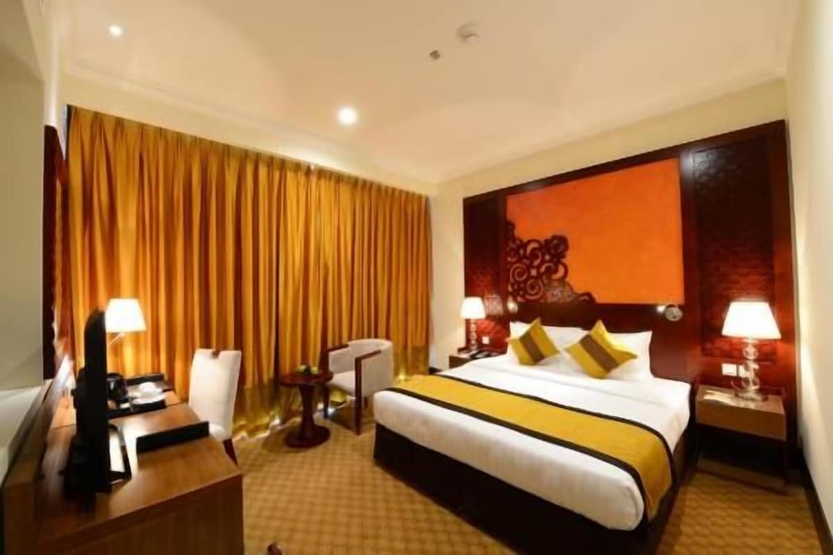 A hotel room with a bed, two bedside tables, a desk, a chair, and a large window with curtains.