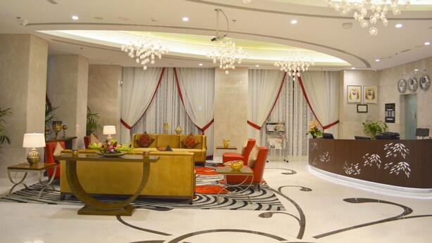 A hotel lobby with a reception desk, seating area, and decorative elements like chandeliers and curtains.