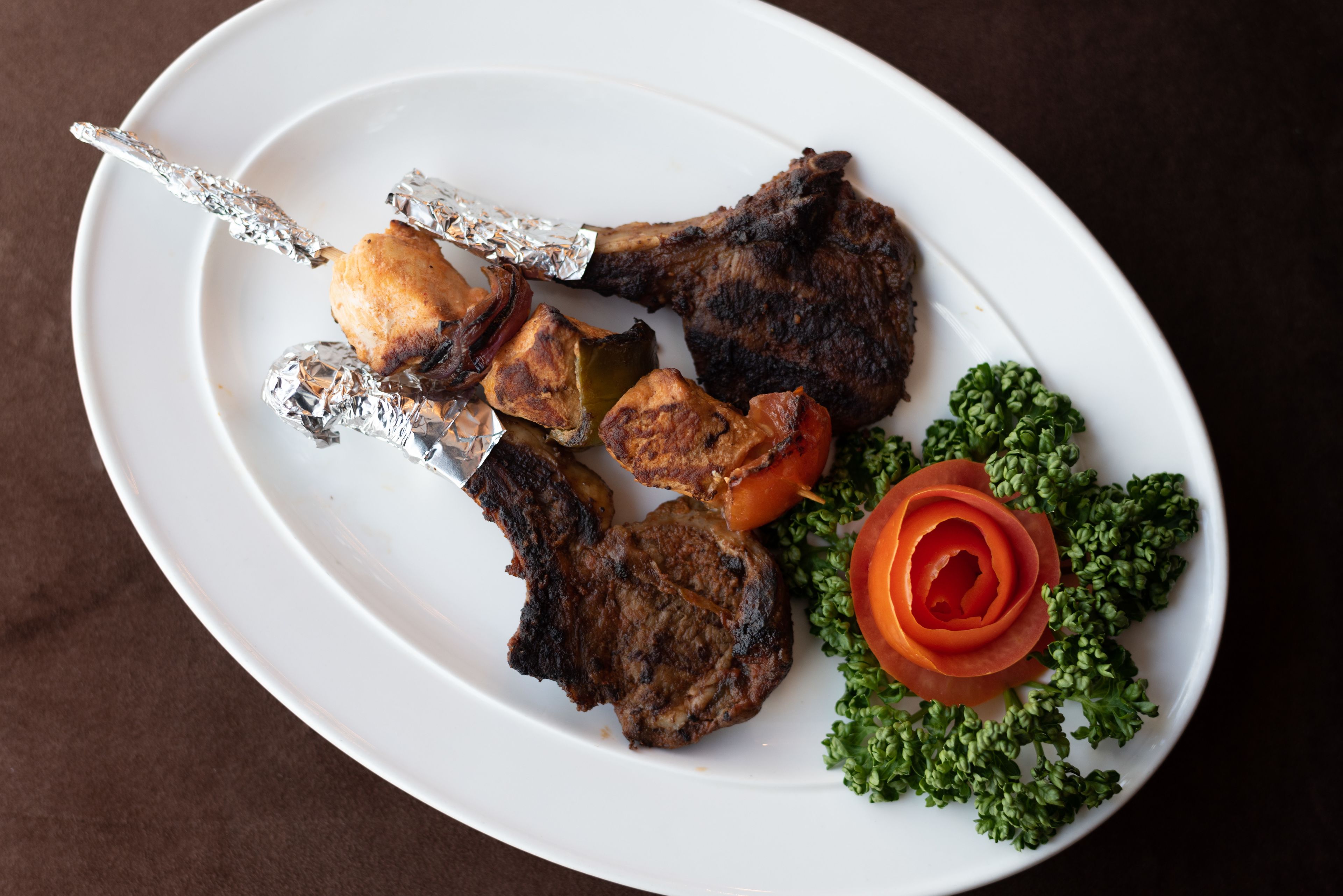 A white plate with grilled meat, vegetables, and a decorative tomato.