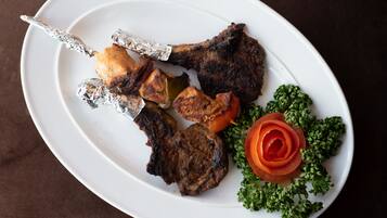 A white plate with grilled meat, vegetables, and a decorative tomato.