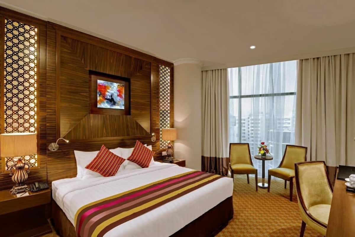 Une chambre d’hôtel avec un grand lit, un téléviseur fixé au mur, un bureau avec une chaise et une vue sur la ville par la fenêtre.