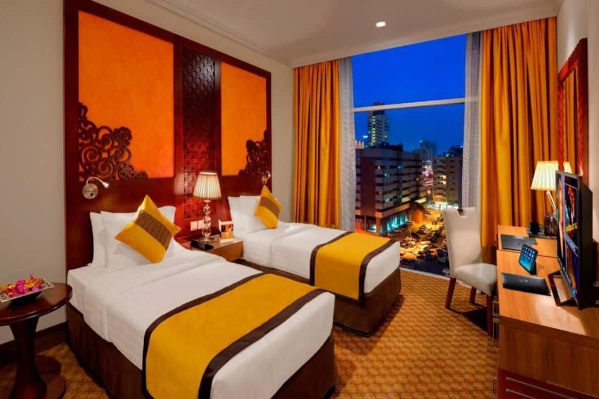 Une chambre d’hôtel avec deux lits, un bureau, une chaise et une vue sur la ville la nuit.