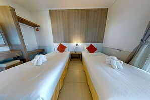 Habitación de hotel con dos camas, una mesita de noche, una lámpara y una ventana con cortinas.