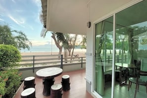 A balcony with a table and chairs, overlooking a beach with palm trees and a fence.