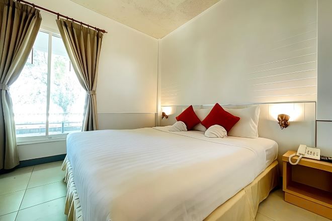 Una camera d'albergo con un letto grande, tende, un comodino con una lampada e una finestra con tende.