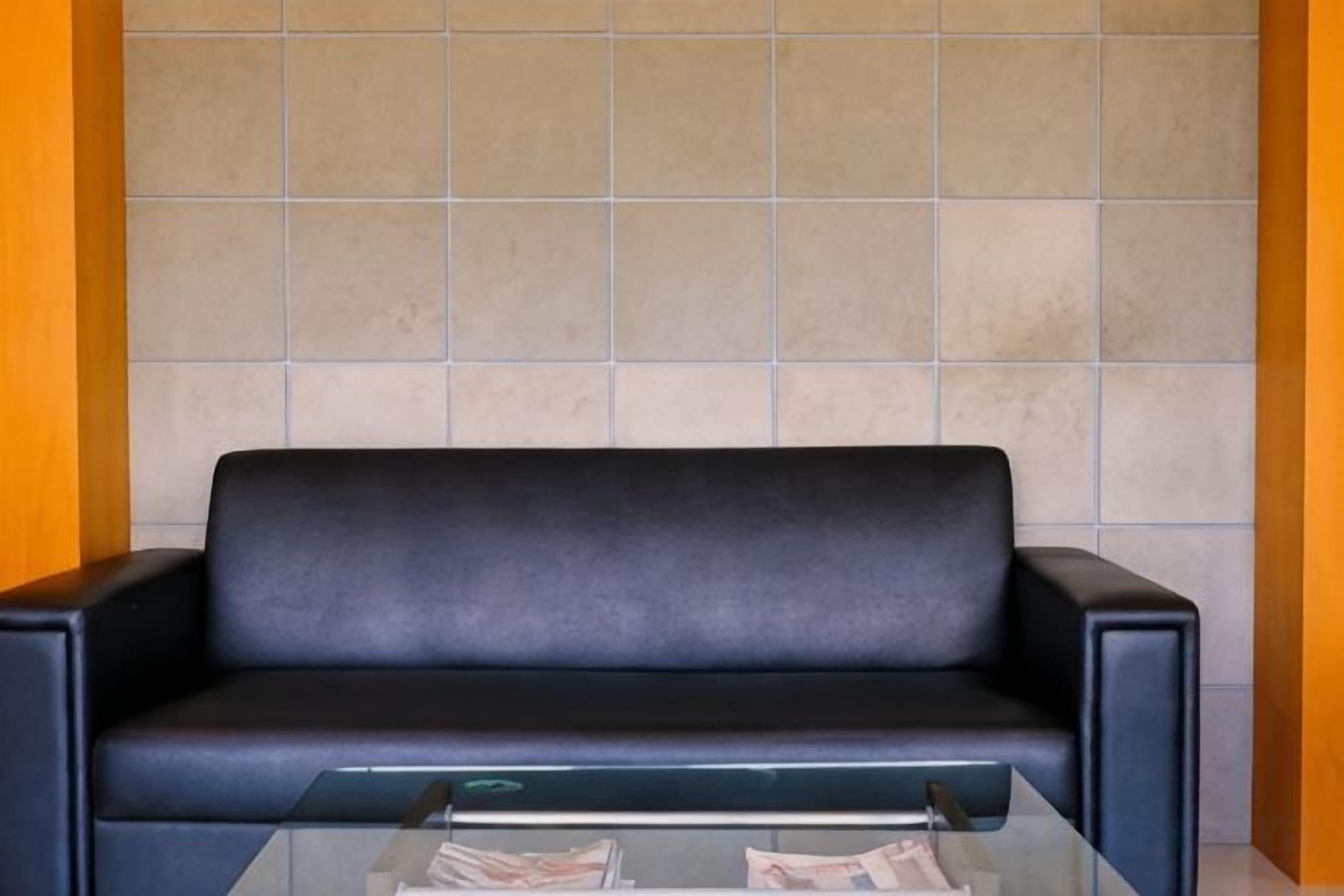 Un sofá de cuero negro con una mesa de centro de vidrio frente a una pared de azulejos.