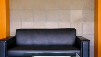 Un sofá de cuero negro con una mesa de centro de vidrio frente a una pared de azulejos.