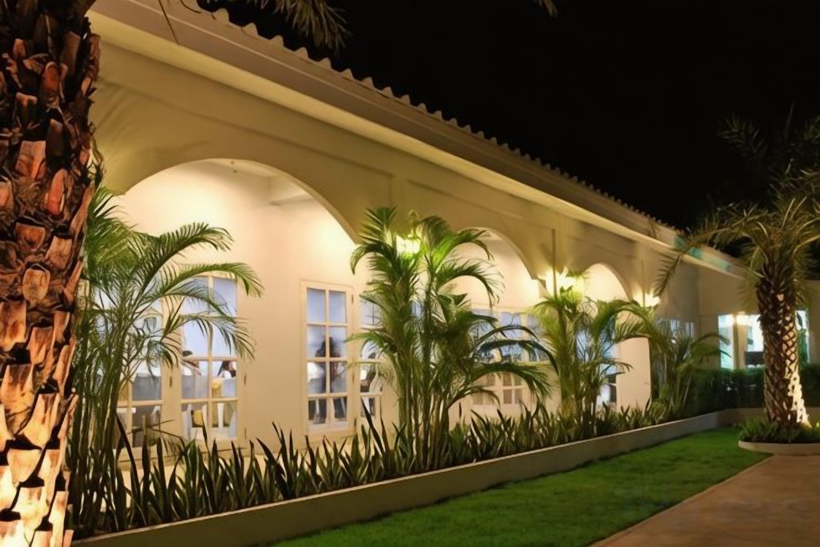 Un edificio con un paseo techado, palmeras y un césped bien cuidado.