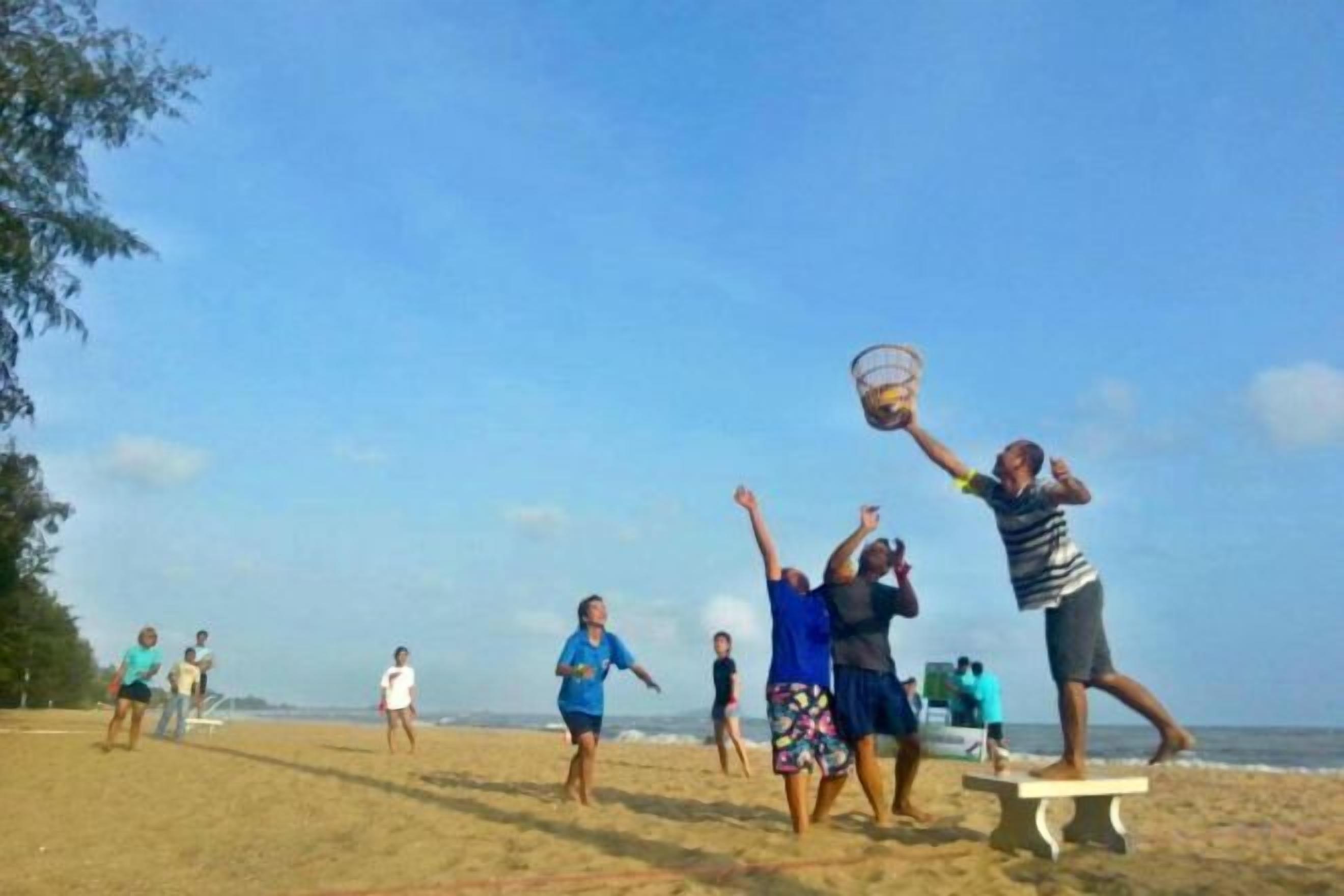 A group of people playing a game on a sandy beach with a clear sky.