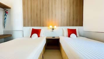 Una habitación de hotel con dos camas, cabecera de madera, lámparas de noche y una mesita de noche.
