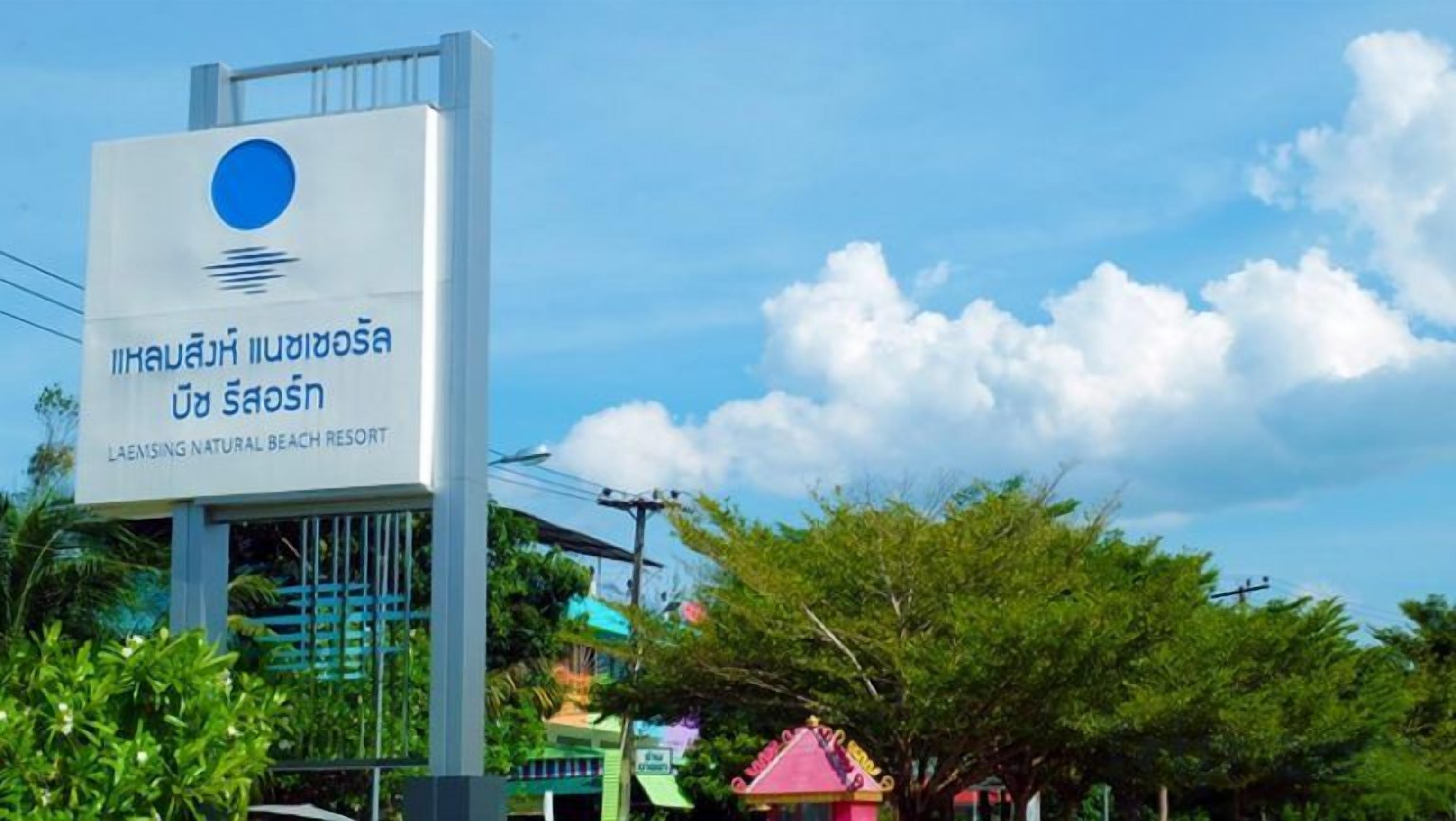 A sign for Laemsing Natural Beach Resort with a clear sky and some trees in the background.