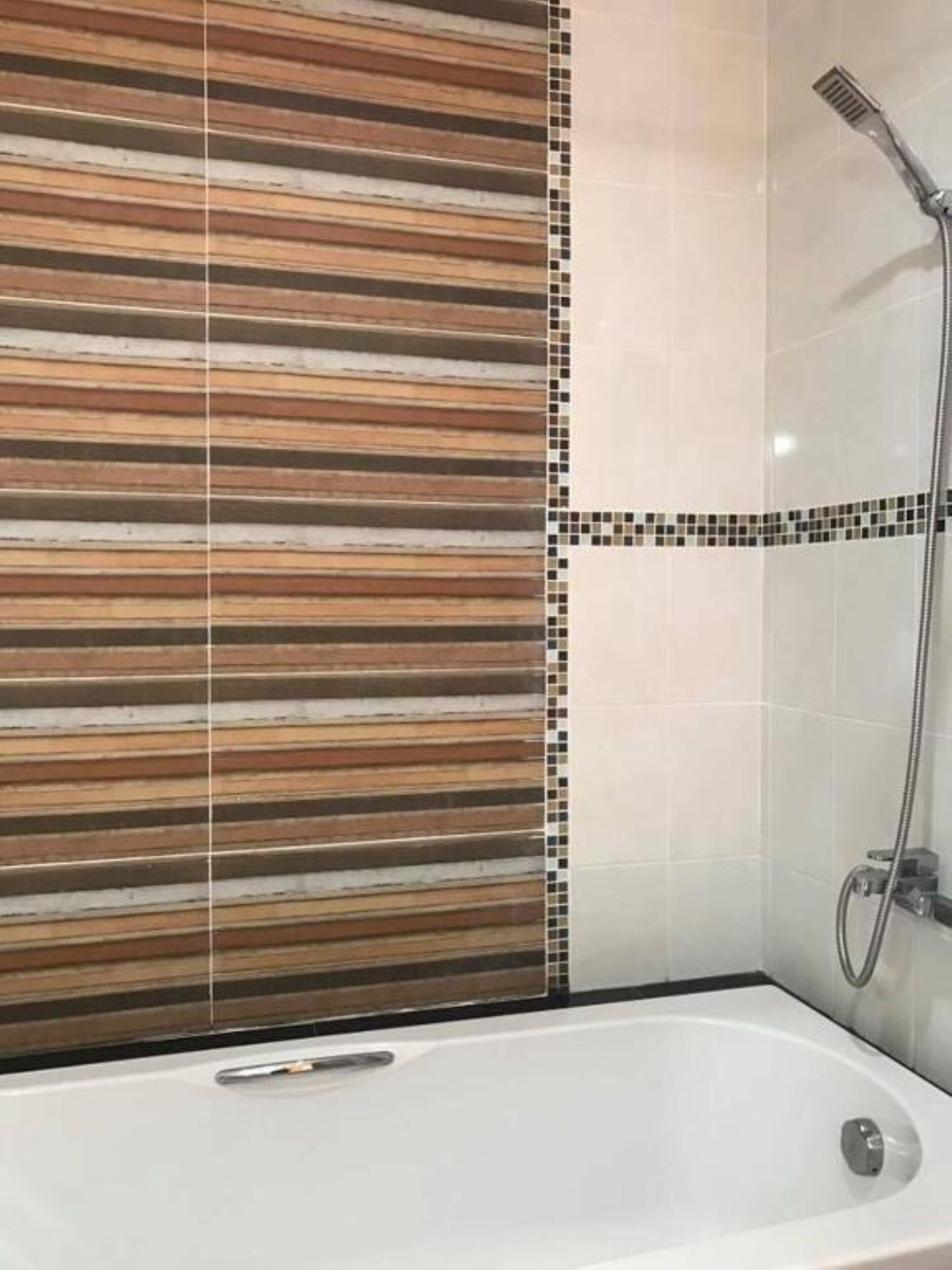 Une salle de bain avec une baignoire, une douche et un mur carrelé orné d’un motif à rayures.