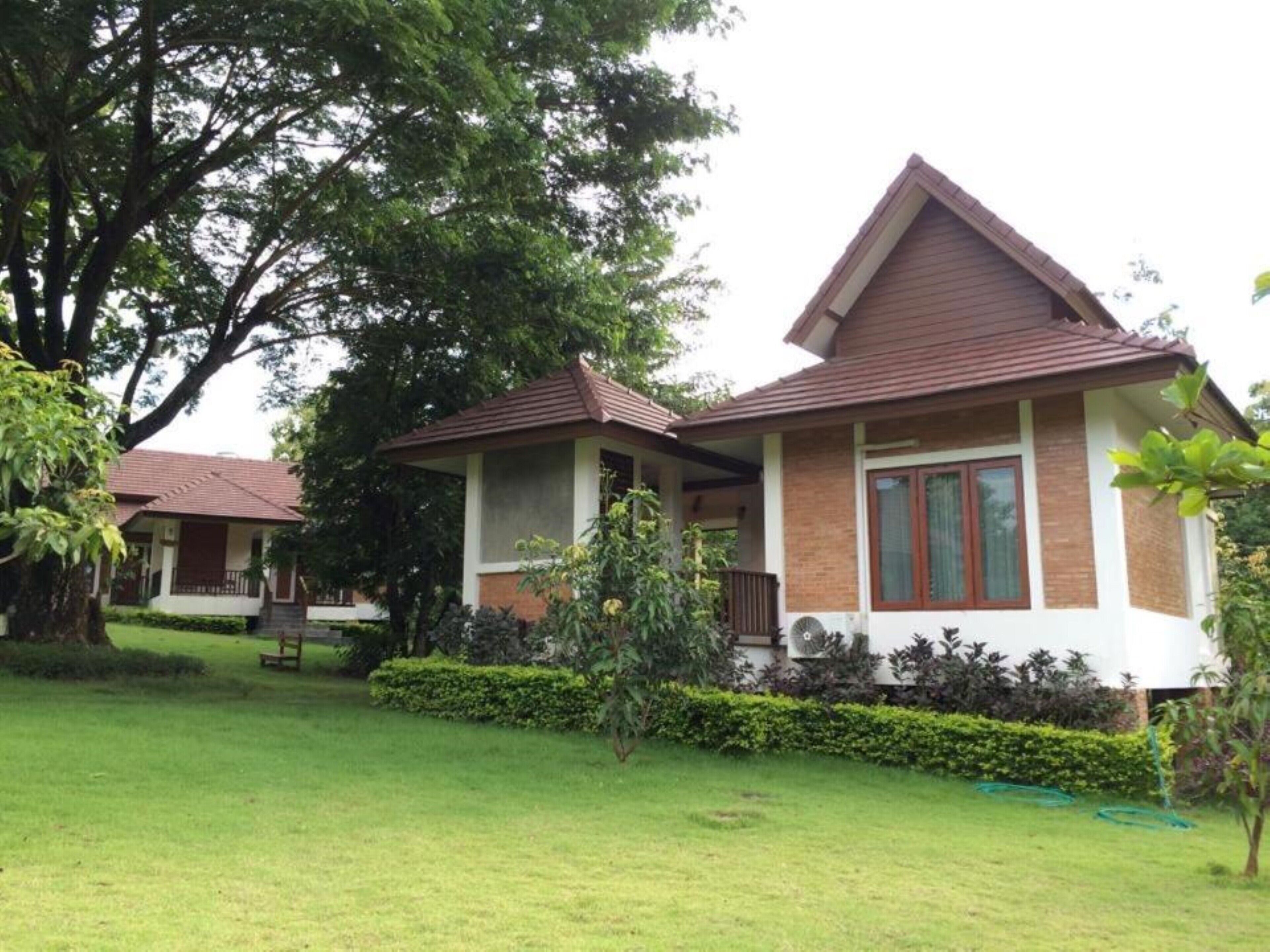 A two-story house with a brown roof and white walls, surrounded by a well-maintained lawn and trees.
