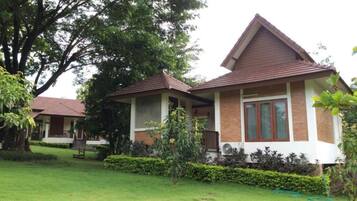 A two-story house with a brown roof and white walls, surrounded by a well-maintained lawn and trees.