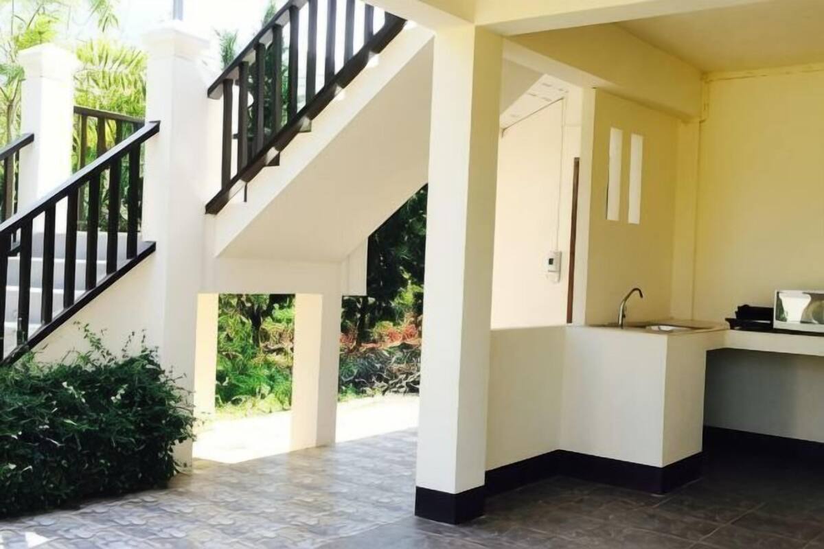 A spacious indoor area with a staircase, a kitchen area, and a door leading to another room.