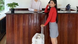 A reception desk with a wooden finish, a large framed artwork depicting a historical scene, and multiple clocks showing different time zones. - Golden Orchid Angkor (Siem Reap)