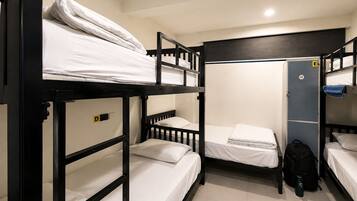 A dormitory room with bunk beds, a wardrobe, and a door marked with an 'E' for emergency exit.