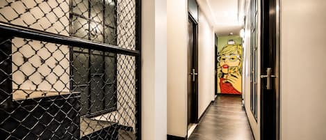 A hallway with a chain-link barrier, a door with a glass panel, and a mural on the wall.