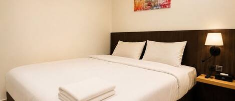 A hotel room with a neatly made bed, a bedside lamp, and a painting on the wall.