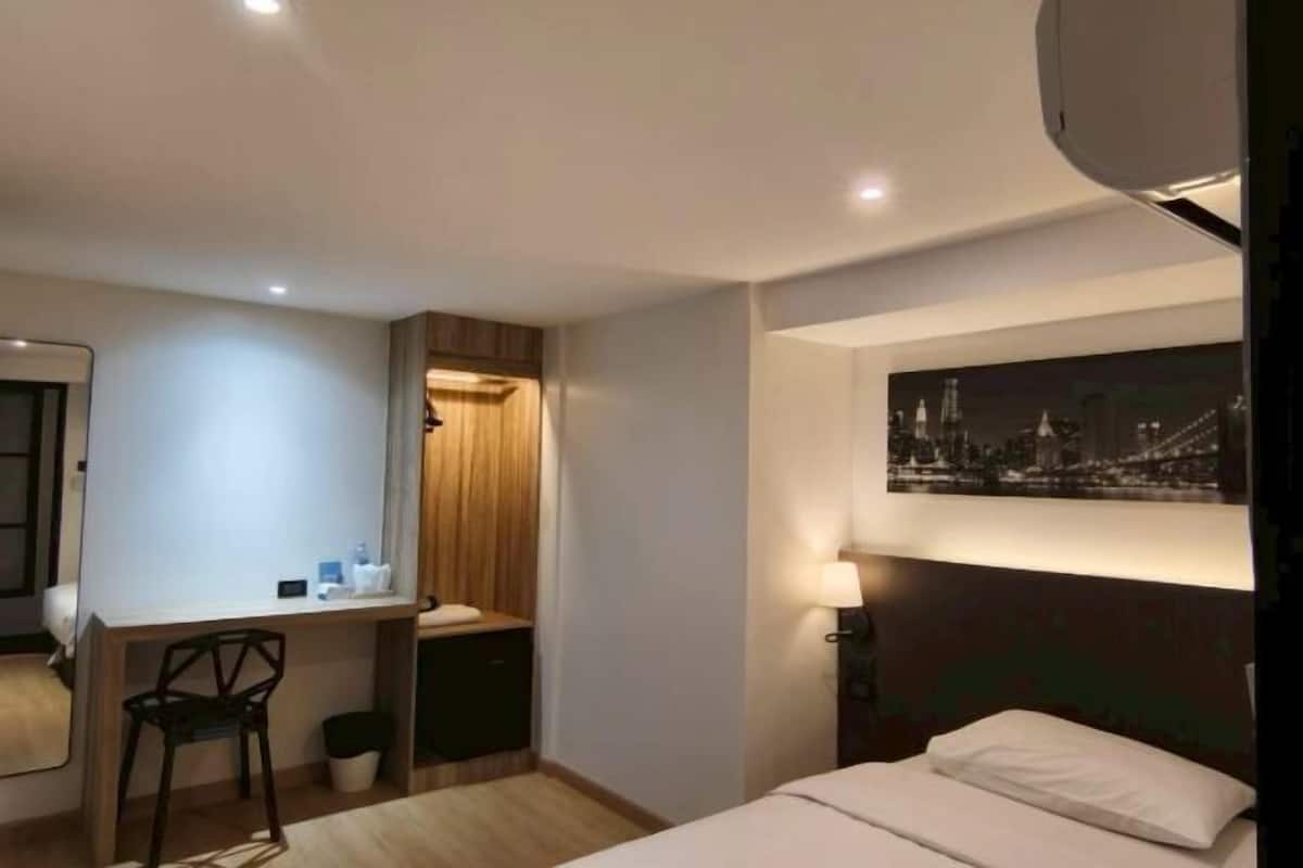 Une chambre d’hôtel comprenant un lit, un bureau, une chaise, un petit placard, une table de chevet et un tableau représentant un paysage urbain.