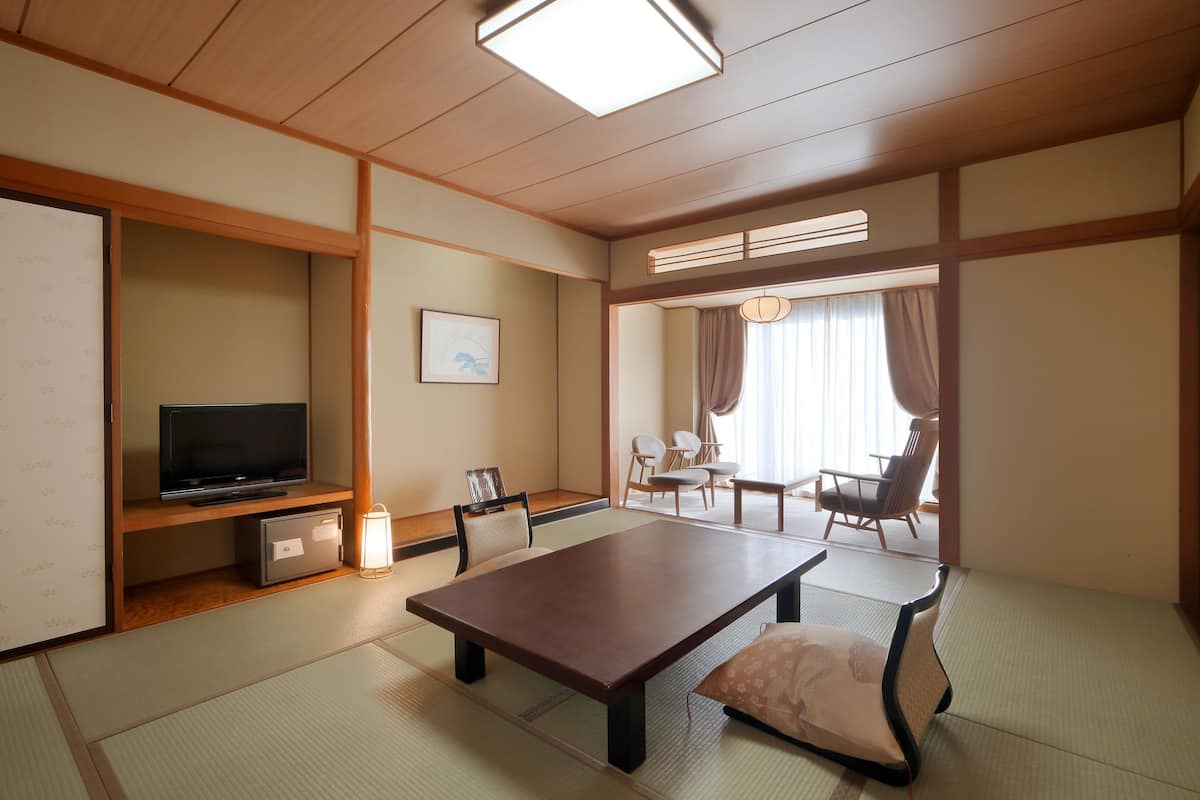 Une pièce de style japonais traditionnel, avec un sol recouvert de tatamis, une table basse, des chaises, un téléviseur et un petit meuble.