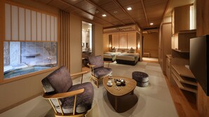 Quarto de hotel moderno com televisão grande, assentos confortáveis, uma mesinha e vista para uma área de águas termais.