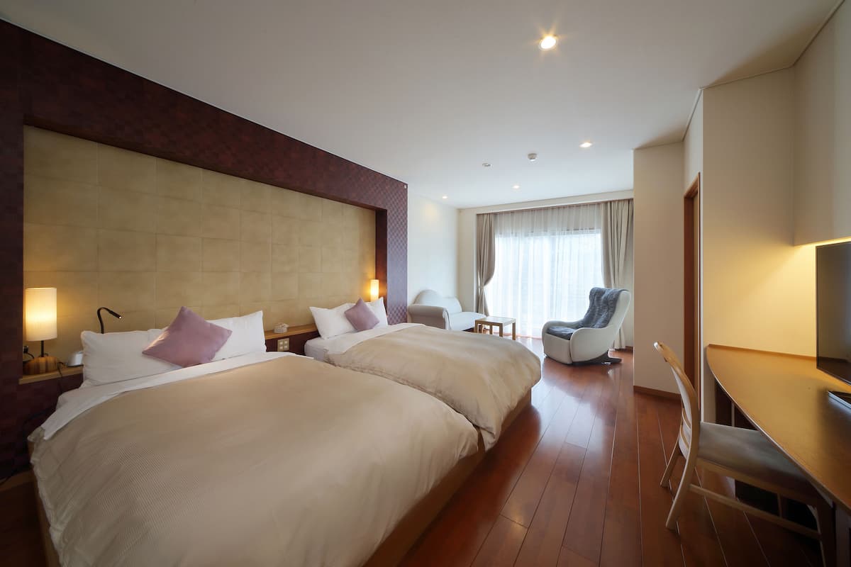 Une chambre d’hôtel avec deux grands lits, un bureau, une chaise et un téléviseur.