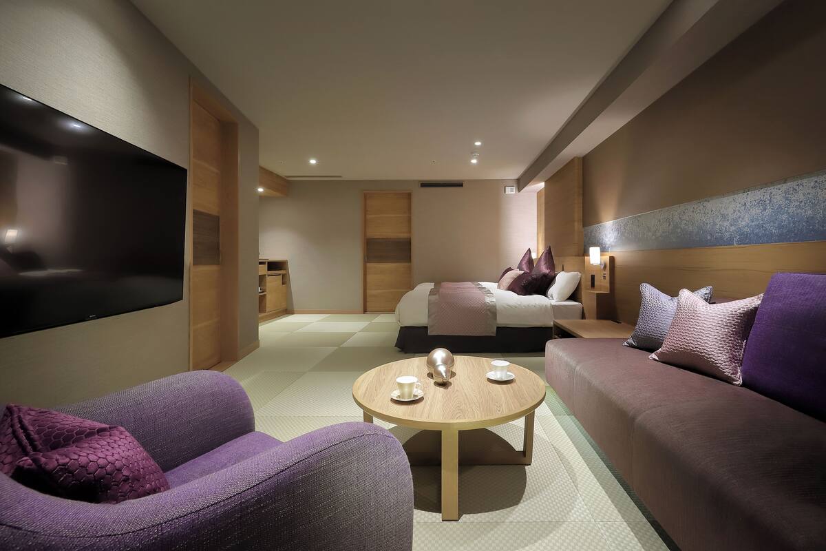 Une chambre d’hôtel moderne dotée d’un grand téléviseur à écran plat, d’un canapé, d’une table basse et d’un lit avec des oreillers.