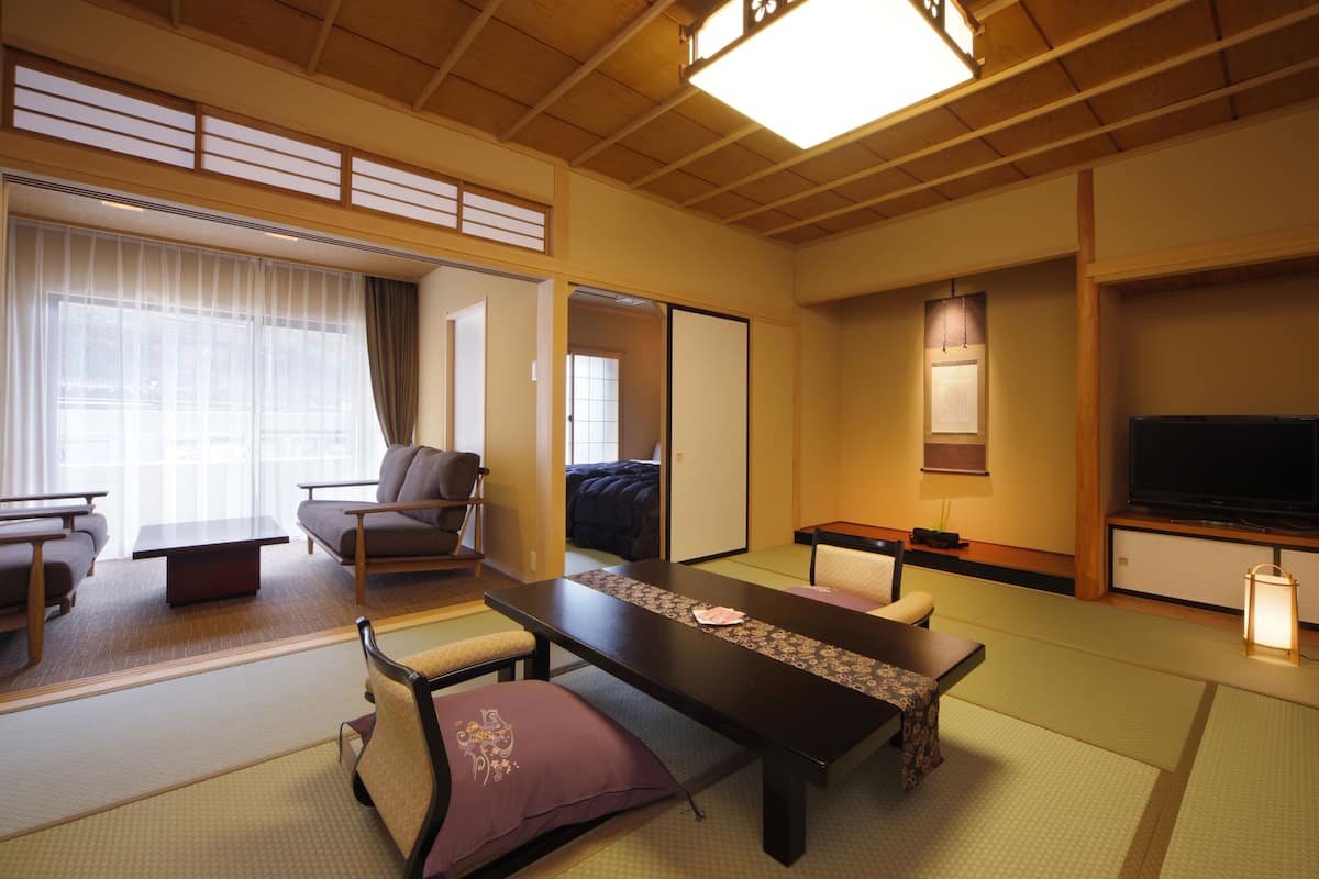 Une pièce de style japonais traditionnel, avec un sol recouvert de tatamis, une table basse, un canapé et un téléviseur.