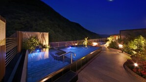 Uma área de piscina no terraço com deck de madeira, degraus que levam à piscina e céu noturno com lua visível.