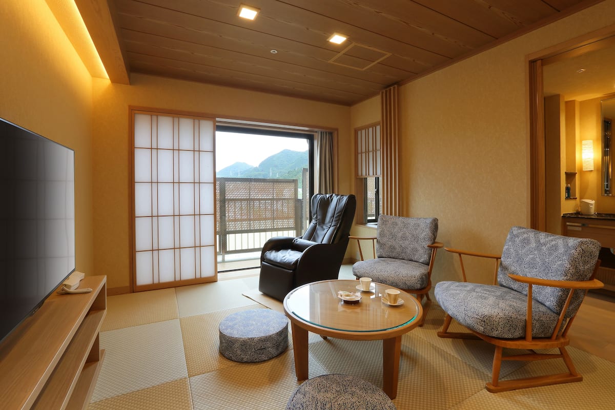 Un salon de style japonais traditionnel, doté d’un sol recouvert de tatamis, d’un téléviseur et d’une porte coulissante donnant sur un balcon.