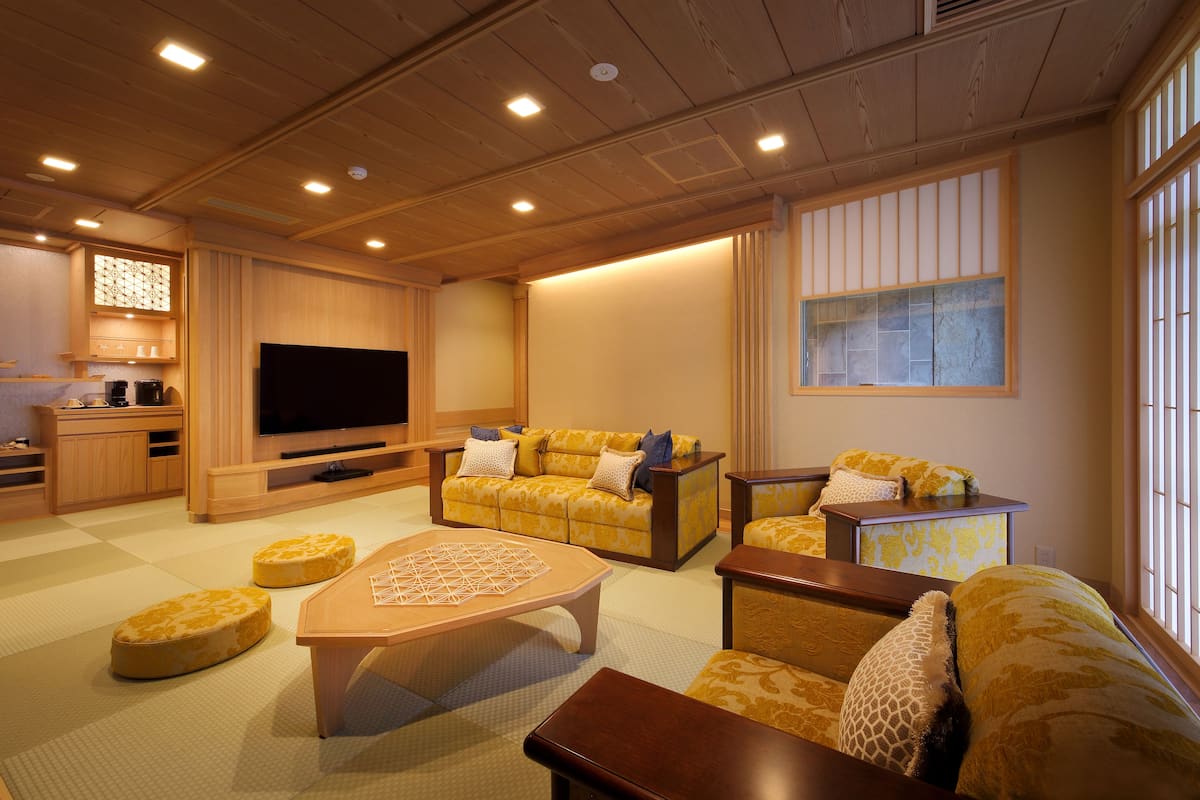 Un salon de style japonais traditionnel, avec un sol recouvert de tatamis, un plafond bas en bois et un grand téléviseur à écran plat.