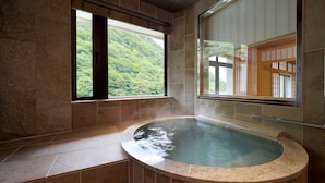 Uma banheira de hidromassagem com vista para uma encosta verde exuberante através de uma janela.