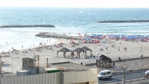 Una playa con sombrillas, un muelle y una camioneta blanca en la carretera.