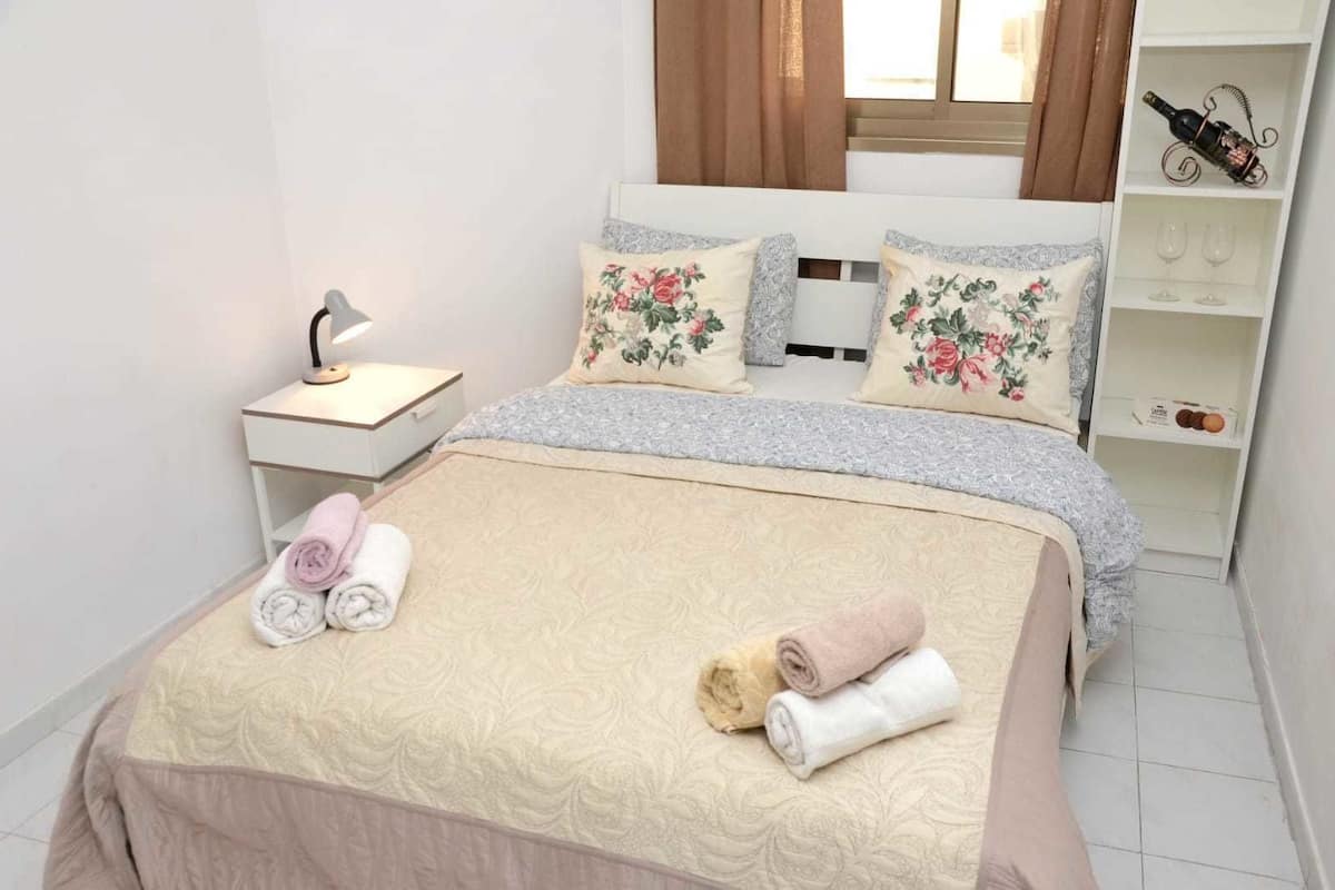 Una cama bien hecha con almohadillas florales y una mesita de noche con una lámpara.