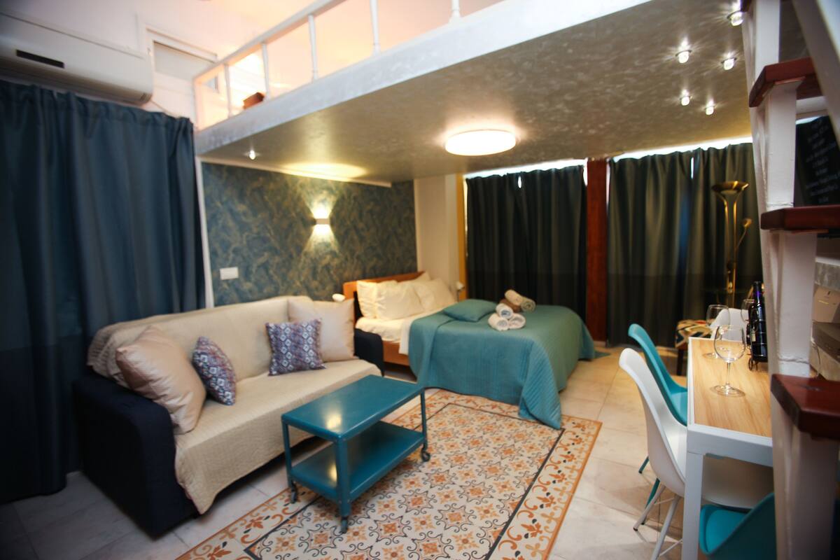 Una habitación de hotel compacta con sofá, cama, una mesita y zona de comedor.