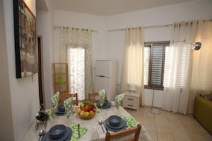 Un comedor con una mesa preparada para cuatro personas, un frutero y un refrigerador al fondo.