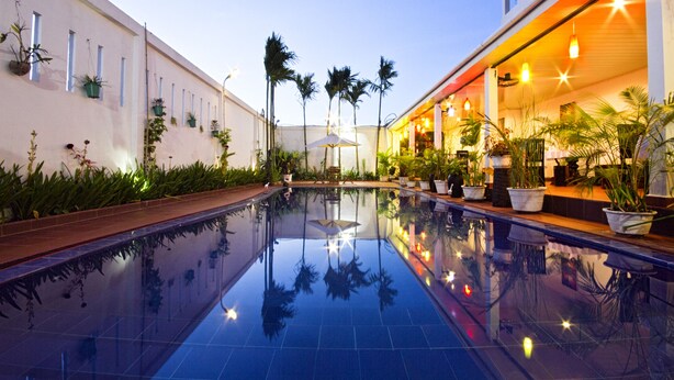 A swimming pool with a reflection of palm trees and a building facade. - Overflow Guesthouse (Siem Reap)