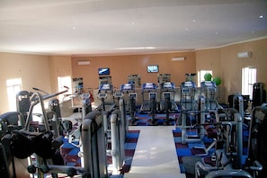 Ein Fitnessstudio mit verschiedenen Trainingsgeräten, einem Laufweg in der Mitte und einem an der Wand montierten Fernseher.