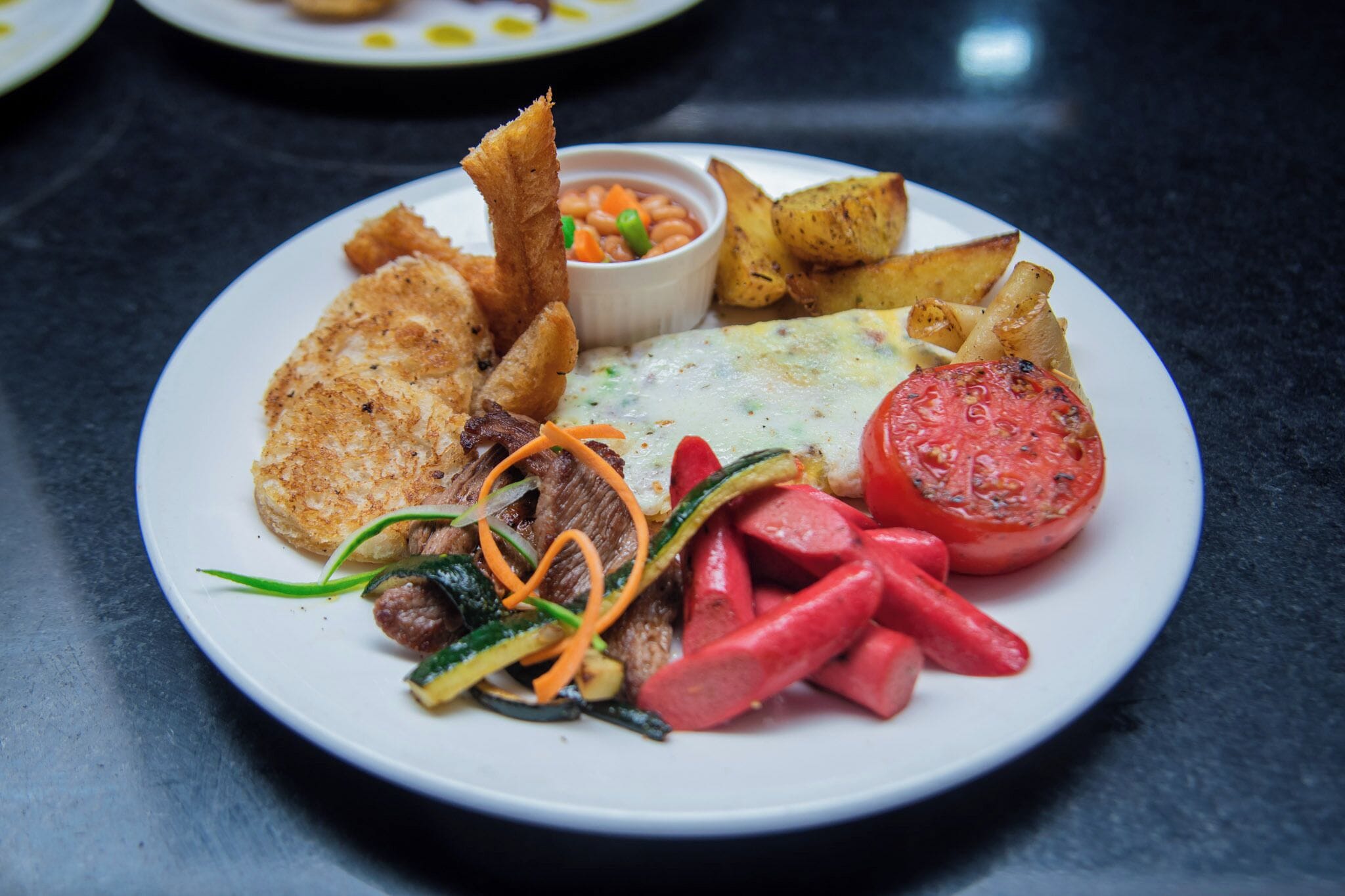 A plate of food with various items including a breaded item, vegetables, and a tomato.