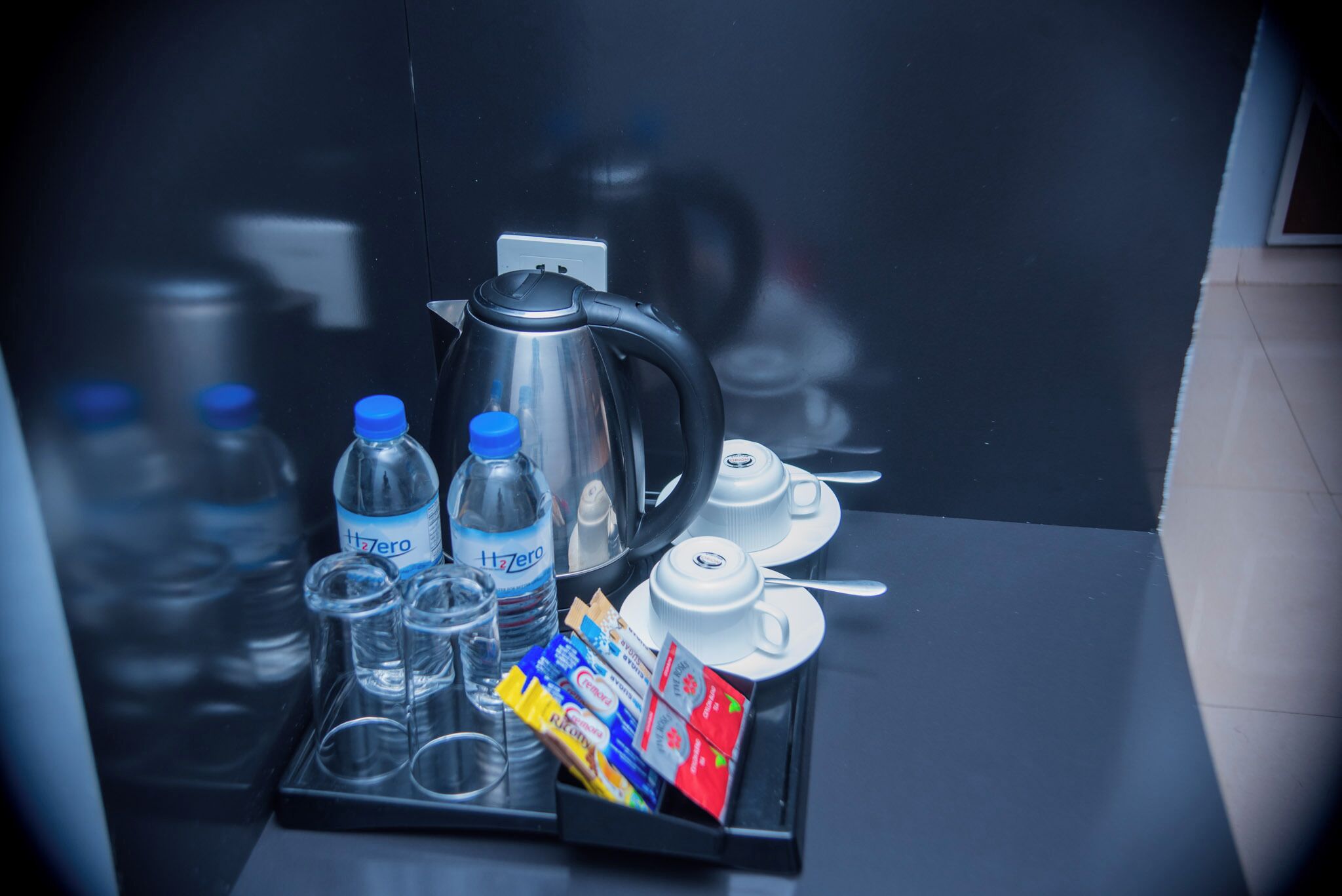 A tray with a kettle, water bottles, glasses, and tea packets on a reflective surface.