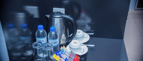 A tray with a kettle, water bottles, glasses, and tea packets on a reflective surface.