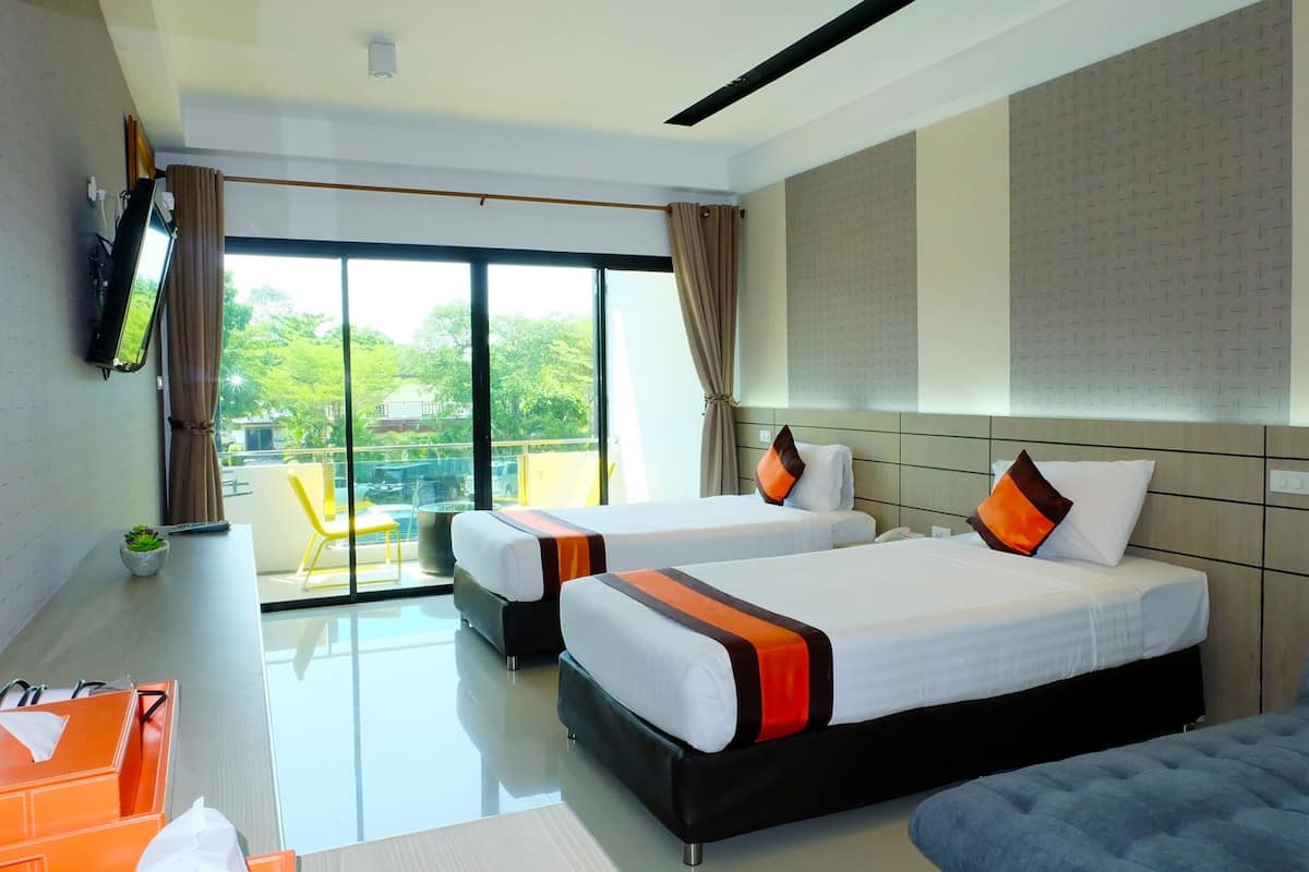 A hotel room with two beds, a TV, a desk, and a balcony with a view of greenery.