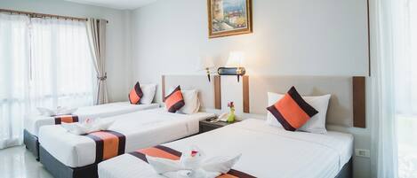 Habitación de hotel con tres camas, cada una con ropa de cama blanca y detalles en naranja, un cuadro en la pared y una lámpara en la mesita de noche.