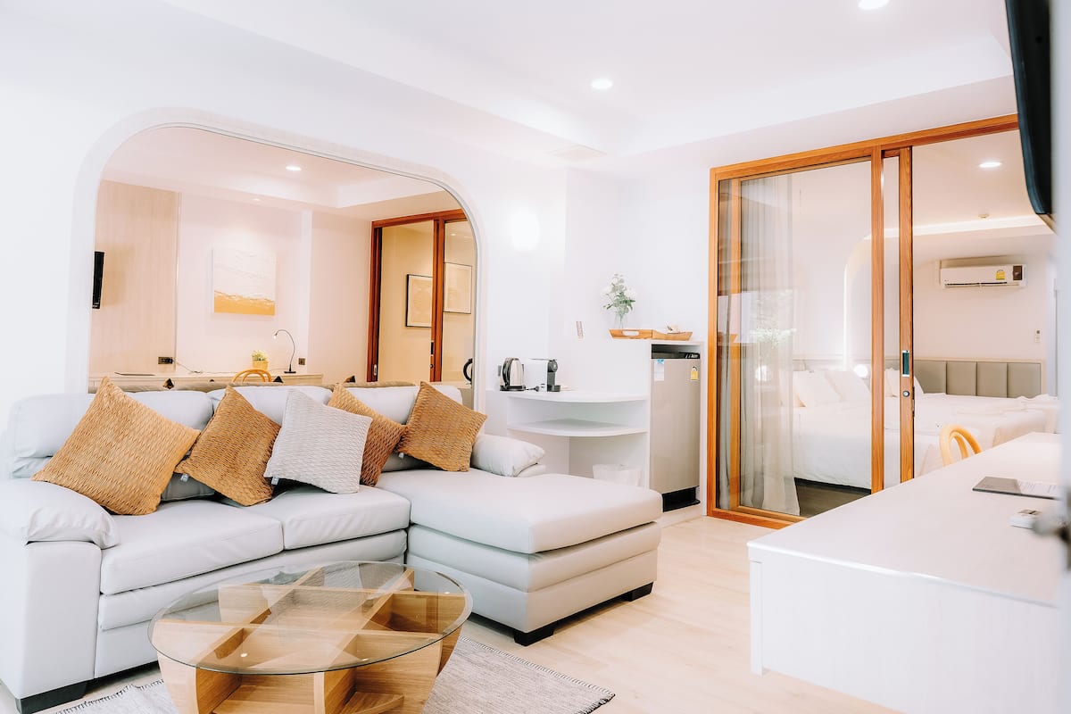 A modern living room with a sectional sofa, a glass coffee table, and a sliding glass door leading to a bedroom.