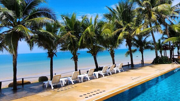 A poolside area with lounge chairs and palm trees, overlooking a beach and ocean.