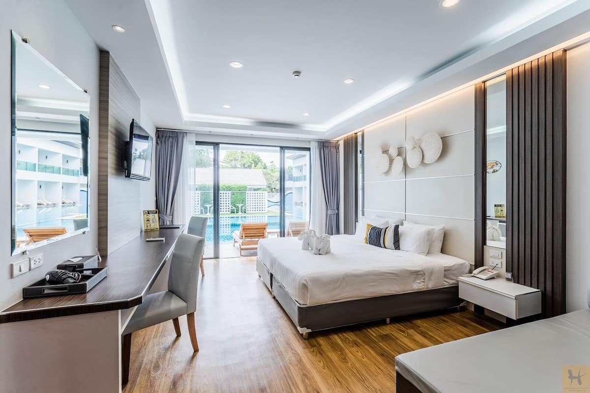 A modern hotel room with a bed, desk, and chair, a large window, and a view of the outdoors.