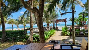 A wooden deck with benches overlooking a beach with lounge chairs and palm trees.