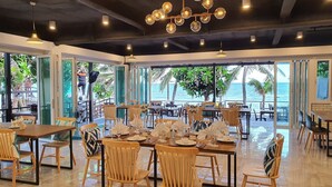 A restaurant with wooden chairs and tables, large windows, and a view of the ocean.